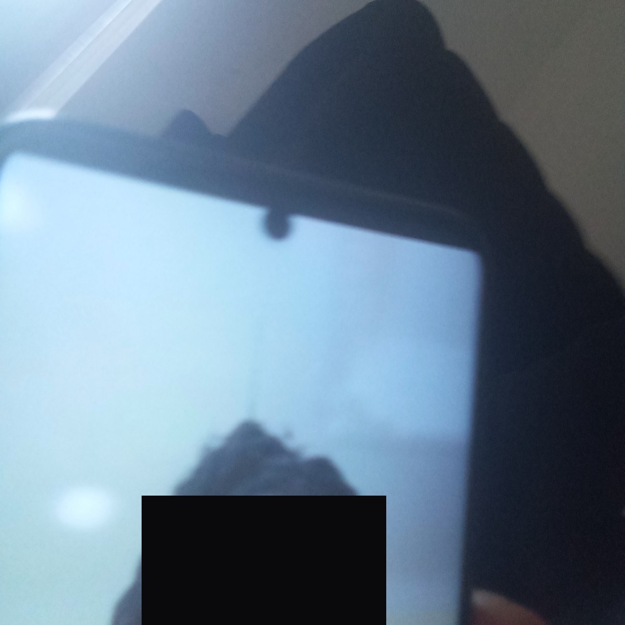 A silent-capture frame of the scammer holding a tablet up to the webcam, playing the stolen photo to fool the face-match — the victim's face redacted