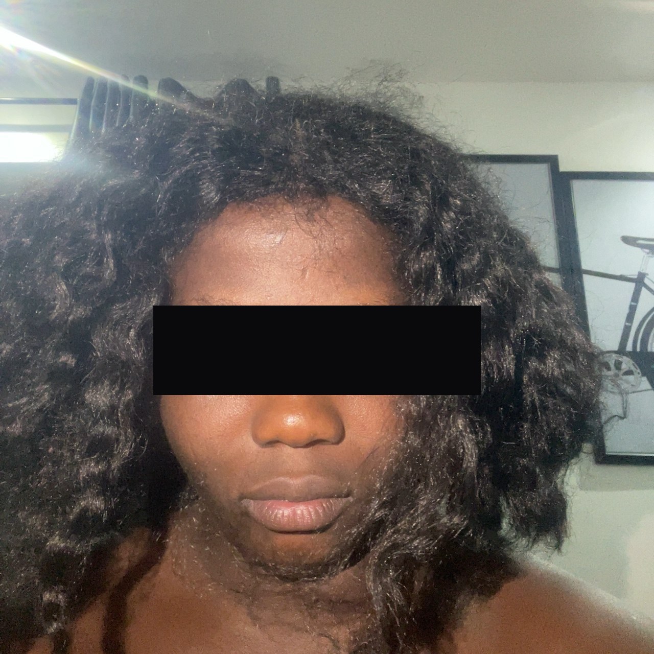 A man wearing a curly wig attempting to pass a face-match verification selfie for a stolen female escort profile — eyes redacted